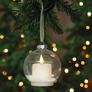 The lighted Snow Globe Candle Ornament lends a quiet elegance with a minimalist feel. The clear ornament bulb contains a battery operated white votive candle that sits on a dusting of sparkling faux snow. The LED candle has a subtle flicker for added ambiance. A flat base allows for freestanding display on a surface, and a light gold ribbon allows for hanging display.