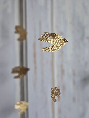 Add a magical touch to any room with our Golden Bird Mobile. The small tin doves appear to float in the air as they hang from golden wires. Features a golden velvet ribbon for hanging.