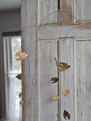 Add a magical touch to any room with our Golden Bird Mobile. The small tin doves appear to float in the air as they hang from golden wires. Features a golden velvet ribbon for hanging.