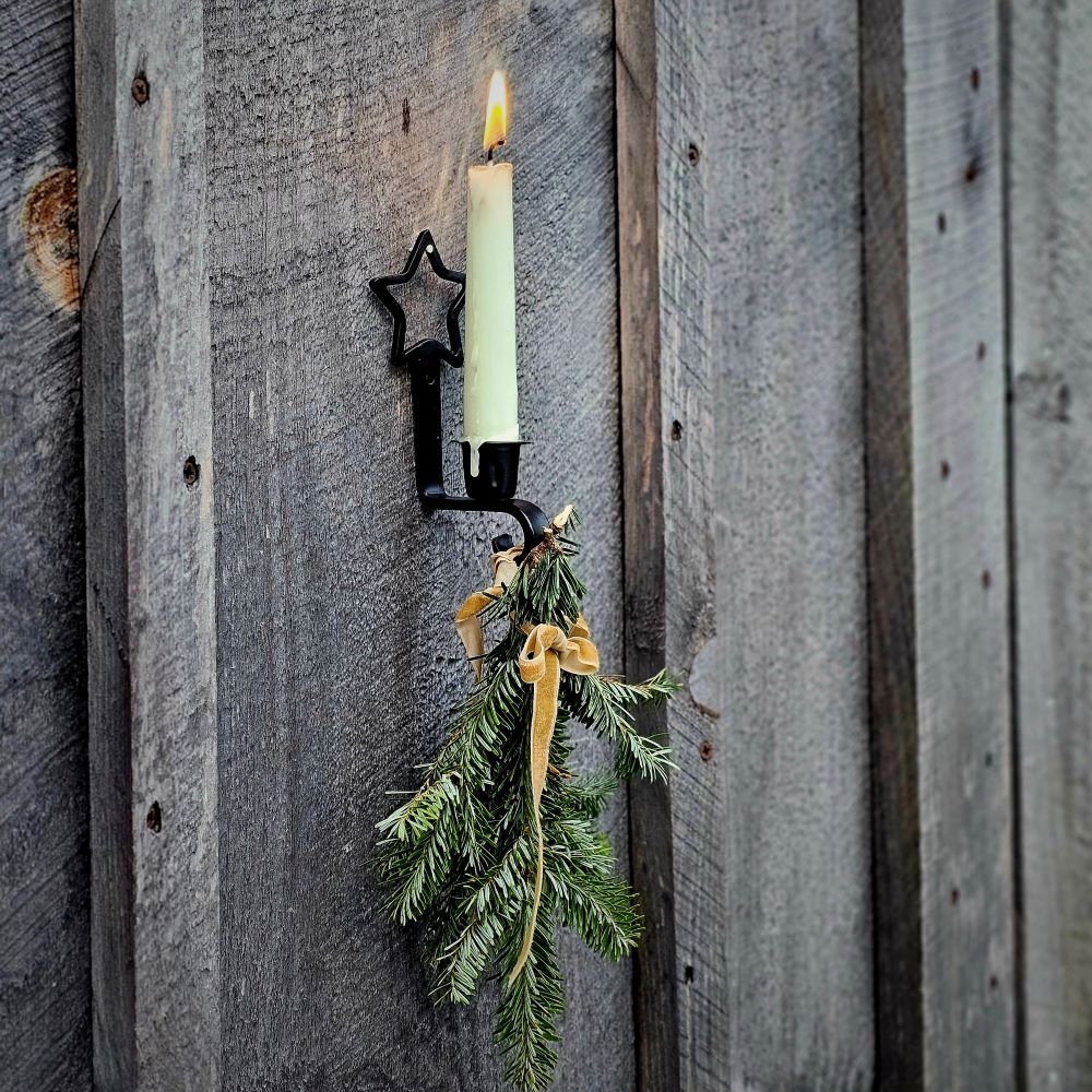 The Primitive Star Taper Candle Sconce with Hook adds a sweet touch to any room. The relaxed design features a metal taper holder with black finish. The top of the holder features a star shape and a pre-drilled hole for hanging. The holder curves up at the base, featuring a small hook for hanging ornaments, candles and more.