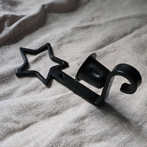 The Primitive Star Taper Candle Sconce with Hook adds a sweet touch to any room. The relaxed design features a metal taper holder with black finish. The top of the holder features a star shape and a pre-drilled hole for hanging. The holder curves up at the base, featuring a small hook for hanging ornaments, candles and more.