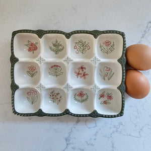 Add vintage style to your kitchen with our Stoneware Egg Tray with Cottage Style. This egg holder is perfect for any farmhouse kitchen. The floral print tray holds a dozen eggs, and is perfect for keeping them close at hand when cooking and baking. It features a dark sage green base with sweet pink cottage flower graphics in each egg cup. This egg holder is also the ideal size  slip into the refrigerator.  Eggs not included. Dishwasher safe. 7.75"L x 6"W x 1.25"H