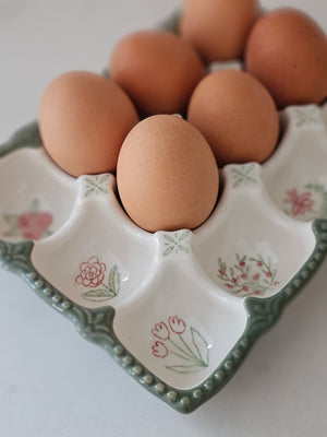 Add vintage style to your kitchen with our Stoneware Egg Tray with Cottage Style. This egg holder is perfect for any farmhouse kitchen. The floral print tray holds a dozen eggs, and is perfect for keeping them close at hand when cooking and baking. It features a dark sage green base with sweet pink cottage flower graphics in each egg cup. This egg holder is also the ideal size  slip into the refrigerator.  Eggs not included. Dishwasher safe. 7.75"L x 6"W x 1.25"H