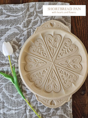 Decorative shortbread pan with heart and flower patterns on a textured surface with a tulip.