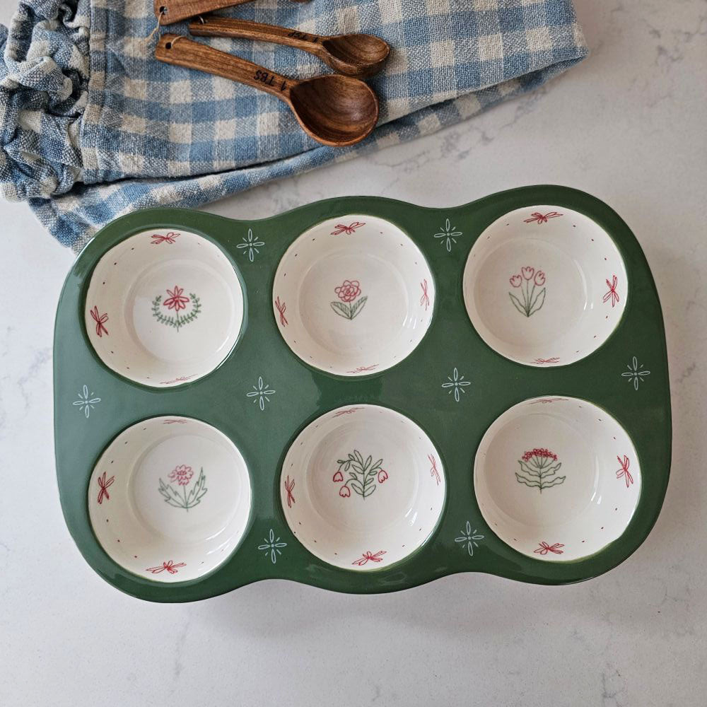 Whether you're baking up something sweet or savory, this Stoneware Muffin Pan with Cottage Style is sure to elevate any recipe. The floral print baking dish holds six muffins or cupcakes. It features a dark sage green base with sweet pink cottage flower graphics in each muffin cup. Dishwasher safe. 12"L x 7.5"W x 1.5"H