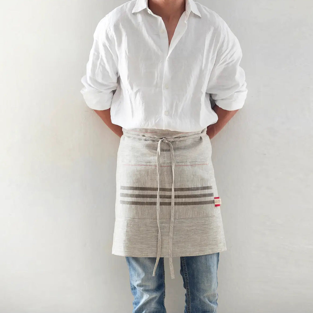 Utility becomes fashionable with our versatile Vintage Line Waist Apron. This kitchen apron is designed to fit women and men comfortably. Sewn out of rustic style linen, this waist apron features grain sack inspired stripes and red stitching. Whether you're cooking up a storm in your farmhouse kitchen, cleaning or grilling with the neighbors, you can protect your wardrobe with this rustic, oatmeal colored linen apron. 