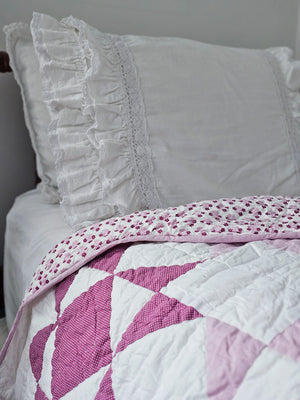 A modern take on the iconic sawtooth star quilt block, this organic cotton patchwork throw is hand quilted by skilled artisans. The antique-inspired design features pinkish-lilac and magenta stars with a playful pin dot pattern. Fully reversible, the quilt backing showcases a coordinating floral print. The Sweet Sawtooth Star Quilted Throw is finished with a playful scalloped binding. Use it to cozy up on the sofa or style it folded at the foot of a twin, full, or queen bed.