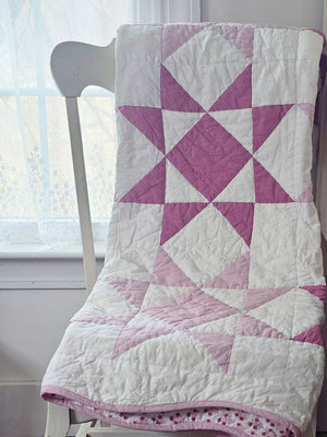 Make this Sweet Sawtooth Star Quilted Throw a treasured heirloom. A fresh take on the iconic sawtooth star quilt block, this organic cotton patchwork throw is hand quilted by skilled artisans. The antique-inspired design features pinkish-lilac and magenta stars with a playful pin dot pattern. Fully reversible, the quilt backing showcases a coordinating floral print. This country classic quilt design is finished with a playful scalloped binding. 