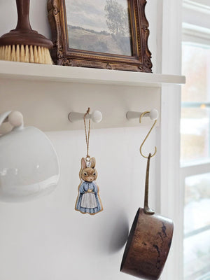 Inspired by Peter Rabbit's mom, this Tea Time Rabbit Ornament lends fairy tale cottage charm to any room. Wearing a classic cottage apron, this bunny is ready for a tea time break. Hang from a hook or from a basket full of your favorite flowers. Image featured on each side of the ornament. 2"L x 4"H