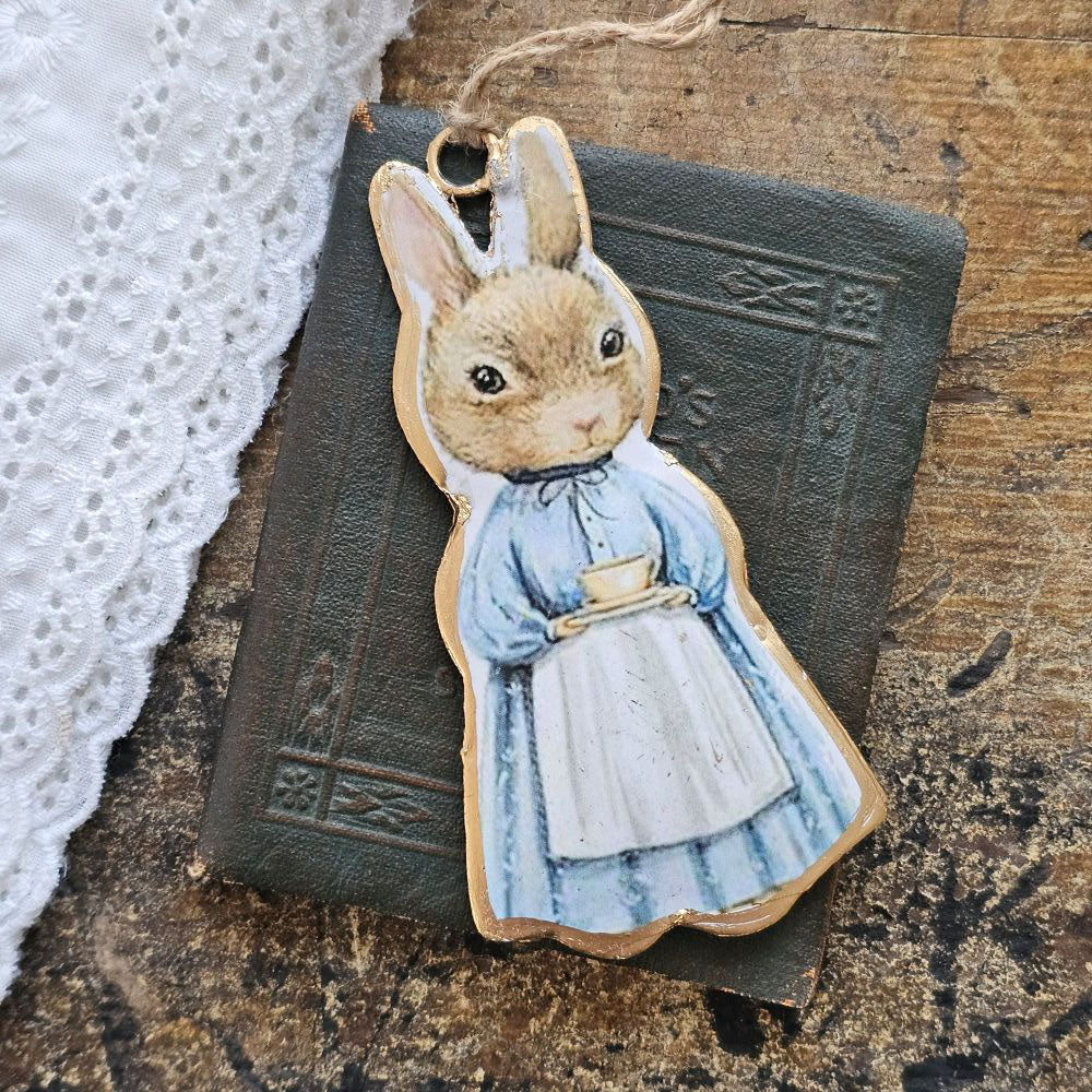 Inspired by Peter Rabbit's mom, this Tea Time Rabbit Ornament lends fairy tale cottage charm to any room. Wearing a classic cottage apron, this bunny is ready for a tea time break. Hang from a hook or from a basket full of your favorite flowers. Image featured on each side of the ornament. 2"L x 4"H