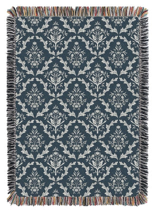 Blue and white floral and thistle patterned throw blanket with black tassels on a wooden surface. Made in the USA