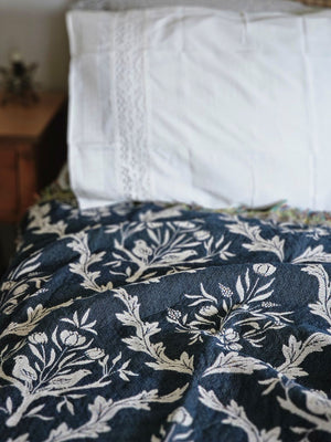 Blue and white floral and thistle patterned throw blanket with black tassels on a wooden surface. Made in the USA