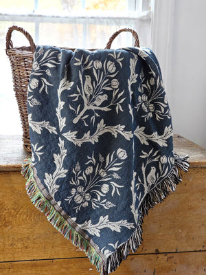 Blue and white floral and thistle patterned throw blanket with black tassels on a wooden surface. Made in the USA