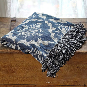 Blue and white floral and thistle patterned throw blanket with black tassels on a wooden surface. Made in the USA