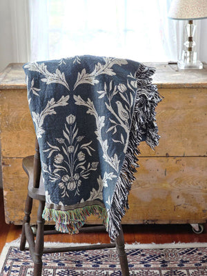 Blue and white floral and thistle patterned throw blanket with black tassels on a wooden surface. Made in the USA