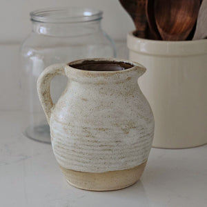 Our Tudor Farm Kitchen Pitcher embodies an old farmhouse aesthetic and Wabi Sabi philosophy—celebrating imperfection, simplicity, impermanence, nature, and uniqueness. Perfect for adding artisanal elegance to any setting. Features a rustic oatmeal color glaze with a natural, non-glazed bottom for an antique and timeless look. Decorative use only. 