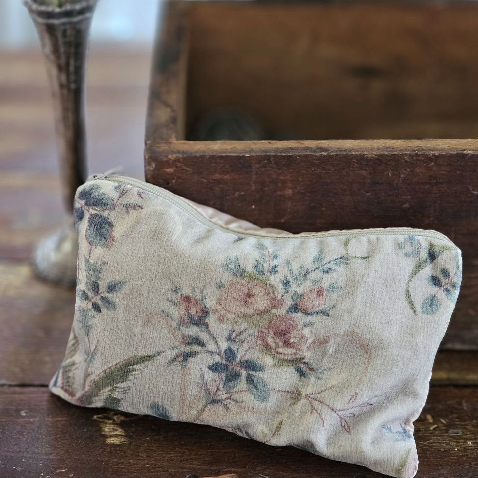 The Velvet Pouch with Vintage Floral Design is an elegant clutch perfect for makeup and other essentials. It showcases a romantic velvet floral pattern on one side, complemented by a smooth light beige-pink satin backside. Measuring 9" wide by 6" high, this zippered pouch combines style with practicality. Print will vary on each bag.