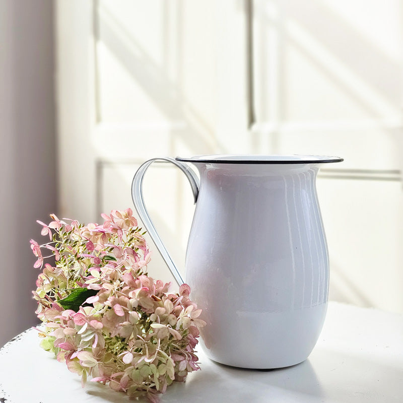 Bring the easy charm of country cottage living to your farmhouse with our Vintage Style Enamel Pitcher with Black Rim. The simple allure of enamelware fits right in with any decor, but every farmhouse needs at least one piece. Inspired by flea market finds, our white enamel pitcher has black trim and makes the perfect vase for your favorite bouquet. Not food safe. Pitcher measures 6¼" high by 5¼" diameter (7" wide with handle).