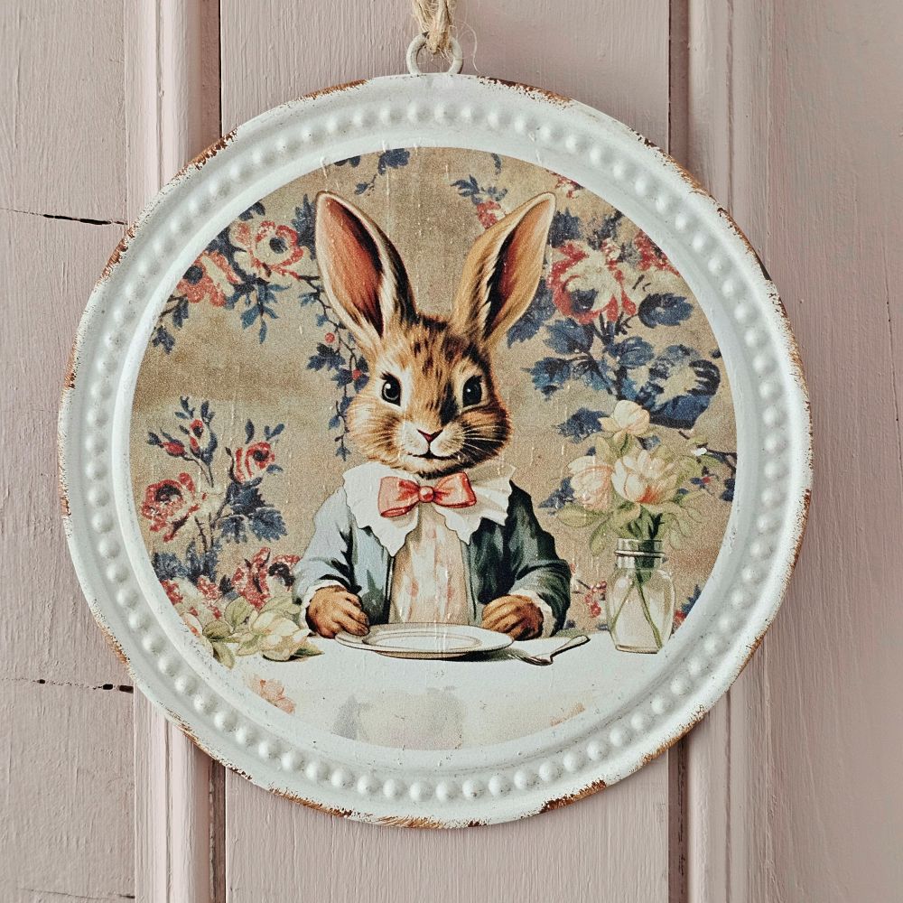 Add sweet cottage style with our Vintage Bunny Distressed Tin Ornament. Who doesn't love a bunny in a bow tie, and the floral wallpaper behind the bunny is adorable. Features and embossed and distressed antique white tin frame and twine for hanging. 5" Diam