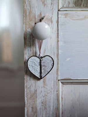 This sweet Vintage Lace Heart ornament captures romantic charm through delicate lace suspended between hand-soldered glass panels. The weathered antique metal frame adds authentic vintage character, while a luxurious satin ribbon provides an elegant finishing touch. Perfect for treasured collections or as a meaningful gift. Lace will vary with each heart, as no two are alike.