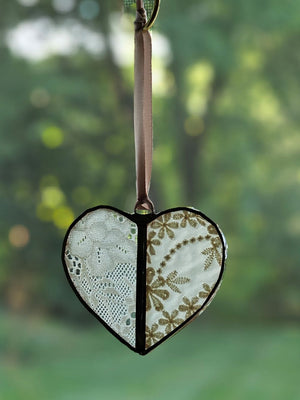 This sweet Vintage Lace Heart ornament captures romantic charm through delicate lace suspended between hand-soldered glass panels. The weathered antique metal frame adds authentic vintage character, while a luxurious satin ribbon provides an elegant finishing touch. Perfect for treasured collections or as a meaningful gift. Lace will vary with each heart, as no two are alike.