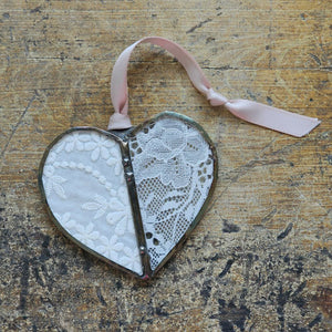 This sweet Vintage Lace Heart ornament captures romantic charm through delicate lace suspended between hand-soldered glass panels. The weathered antique metal frame adds authentic vintage character, while a luxurious satin ribbon provides an elegant finishing touch. Perfect for treasured collections or as a meaningful gift. Lace will vary with each heart, as no two are alike.