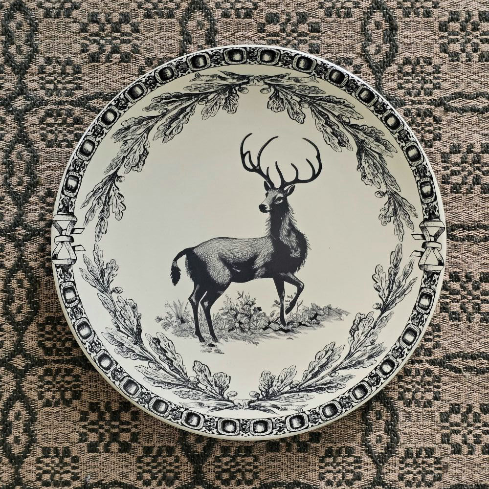 This stoneware Vintage Style Deer Plate features an elegant deer motif framed by delicate branch and acorn patterns, inspired by timeless old-world decor. Antique white with black details, it has a coordinating border design adds a refined touch, making it ideal for both everyday meals and special seasonal gatherings. Crafted for convenience, the plate is microwave, oven, dishwasher, and food safe, blending rustic charm with practical functionality. Includes one plate. 8" diam