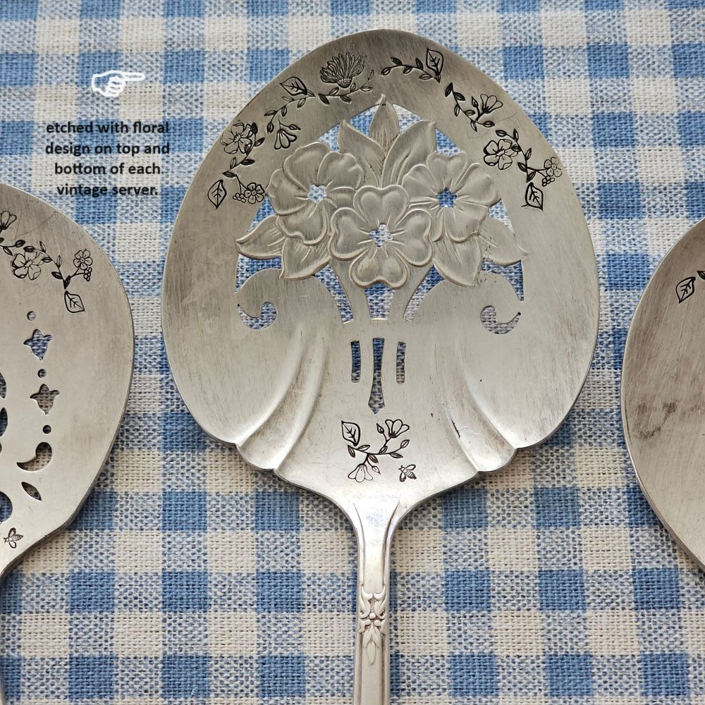 Darling Vintage Tomato Servers are hand-stamped with a floral design along the top and bottom of each server. Made from vintage silver plate servers, each item will be unique. Due to their vintage nature, flatware pieces may show signs of age and gentle use. No two are alike and the face and handle will vary. The servers are all lovingly collected by the artist from flea markets and antique shops and then hand-stamped with care. Includes one tomato server. Each approximately 8"L. Made in the USA.&nbsp;