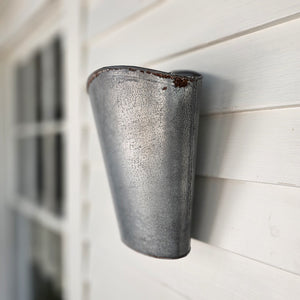 With plenty of cottage style charm, our Weathered Galvanized Wall Bucket offers a rustic touch to any room. It has hearty aged character and is perfect for floral displays. The wall-mounted bucket, has bits of rust, giving it a weathered and worn look. It dresses up any room with vintage farmhouse style. Can also sit on a tabletop. Flowers sold separately. 9″L x 4.8″W x 11.3″H