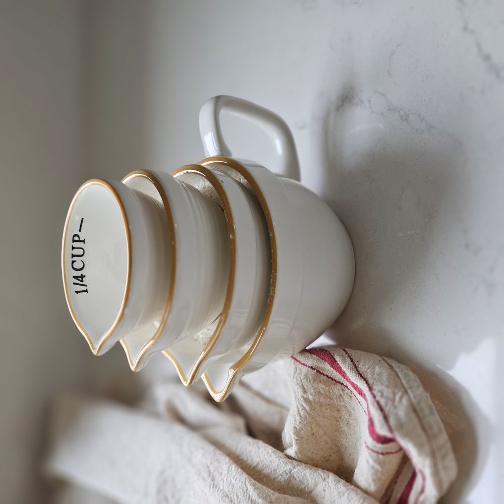 The perfect tool for any farmhouse kitchen, this set of four White Ceramic Nesting Measuring Cups features a creamy white finish with rustic golden tan rims. Each cup has a spout for easy pouring. Set of four includes 1 cup, 1/2 cup, 1/3 Cup and 1/4 cup. Microwave, dishwasher and oven safe.