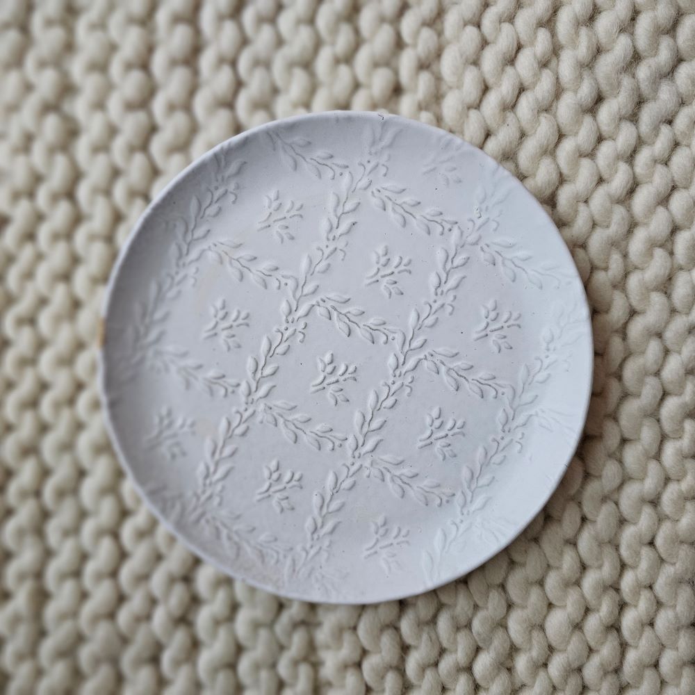 Add cheerful country style with our White Ceramic Embossed Plate. Made of ceramic, this durable plate displays a white glaze finish with embossed patterns of plant vines on the inside of the plate. Embossed vine designs come through the glaze for textured detail. Perfect for holding trinkets and jewelry or use as a soap dish. Includes one plate. Each sold separately. Hand wash