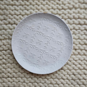 Add cheerful country style with our White Ceramic Embossed Plate. Made of ceramic, this durable plate displays a white glaze finish with embossed patterns of plant vines on the inside of the plate. Embossed vine designs come through the glaze for textured detail. Perfect for holding trinkets and jewelry or use as a soap dish. Includes one plate. Each sold separately. Hand wash