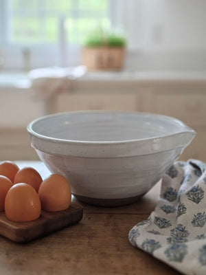 The White Farmhouse Mixing Bowl has a clean, simple design that will help you whip up a farmhouse style pancake breakfast and other goodies. It features a rustic hand-thrown pottery look with pour spout. The whitewash glaze and unglazed bottom add to its rustic feel. This sturdy bowl is perfect for every day living. Food safe. Hand wash recommended. Wood spoon sold separately. 9.5" Diam x 4.75"H