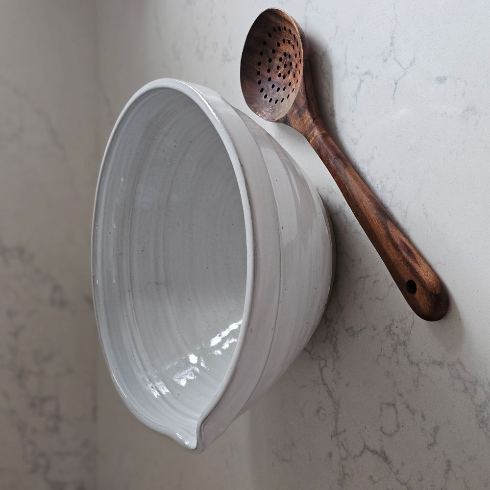 The White Farmhouse Mixing Bowl has a clean, simple design that will help you whip up a farmhouse style pancake breakfast and other goodies. It features a rustic hand-thrown pottery look with pour spout. The whitewash glaze and unglazed bottom add to its rustic feel. This sturdy bowl is perfect for every day living. Food safe. Hand wash recommended. Wood spoon sold separately. 9.5" Diam x 4.75"H