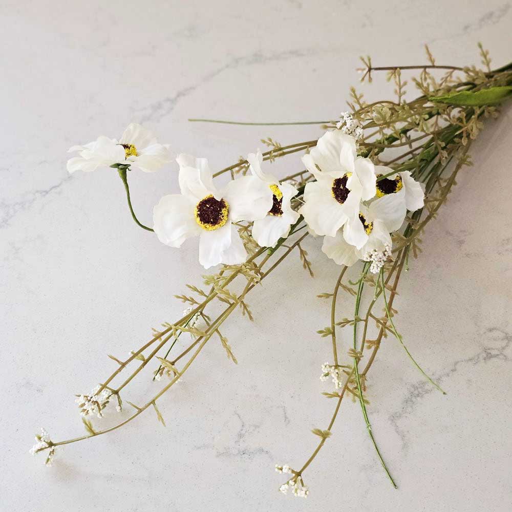 Farmhouse cottage style is made easy with our White Wildflower Spray Pick. This faux flower spray features creamy white fabric petals with brown and yellow pistil centers for a realistic touch. Fresh green leaves on a plastic green stem complete this floral. The stem is long, slender, and flexible and is easily shaped for a desired look. It can be displayed alone for a simple country look or arranged into a bouquet. It easily fits into baskets, buckets, and milk cans and more.