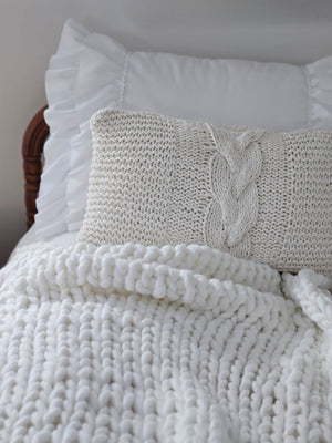 White knitted blanket and pillow on a bed with white pillows