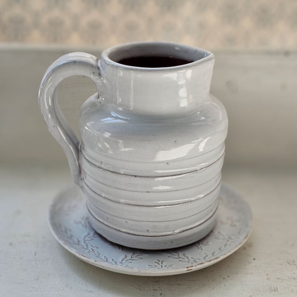 The Whitewash Stoneware Ribbed Pitcher offers rustic charm with its simple design. Features a dreamy white glaze over earthy stoneware. Hints of clay tones peek through the ribbed design. It makes the perfect accent for a bedside table, bookshelf or use it as a vase to create a farmhouse centerpiece. 5"Diam x 5"H.