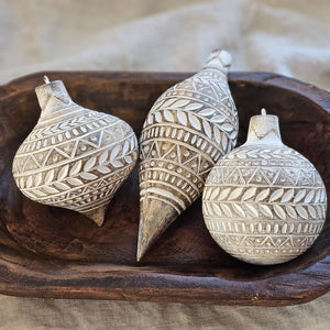 These decorative Distressed White Carved Wood Style Ornaments add a unique touch to bowls and displays. Like snowflakes, each has a different festive white design that really pops against the underlying rustic wood color grain. Includes metal loop for hanging. Made of resin/stonepowder. Set of three