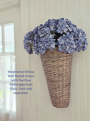Weathered Willow Wall Basket with Blue Hydrangea Bushes against a white wall.