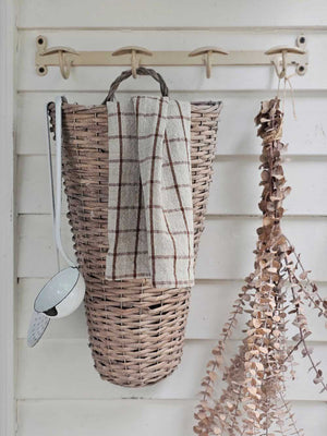 Wicker basket with a plaid towel hanging on a wooden rack against a white wall.