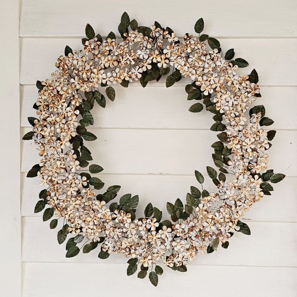 The Winter Meadow Metal Wreath is an everlasting statement piece. Dramatic in scale and intricate in its attention to detail, the vintage inspired Winter Meadow Metal Wreath is elaborately crafted by hand. Each leaf and delicate white flower are hand cut and formed to create a lasting piece for your entryway, mantel, or wherever your creativity guides you to grace it. Rust is intentional and part of the intrinsic nature and beauty of this product.. Crafted of iron with rusted metal flowers and dark green me