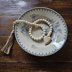 This Wood Bead Rope with Carved Heart adds texture and style to hooks and shelves. This hanging heart features natural wood beads and a simple small, natural wood heart and a twine tassel. Perfect for wood and white farmhouse decor. 1.5" W x 26"H