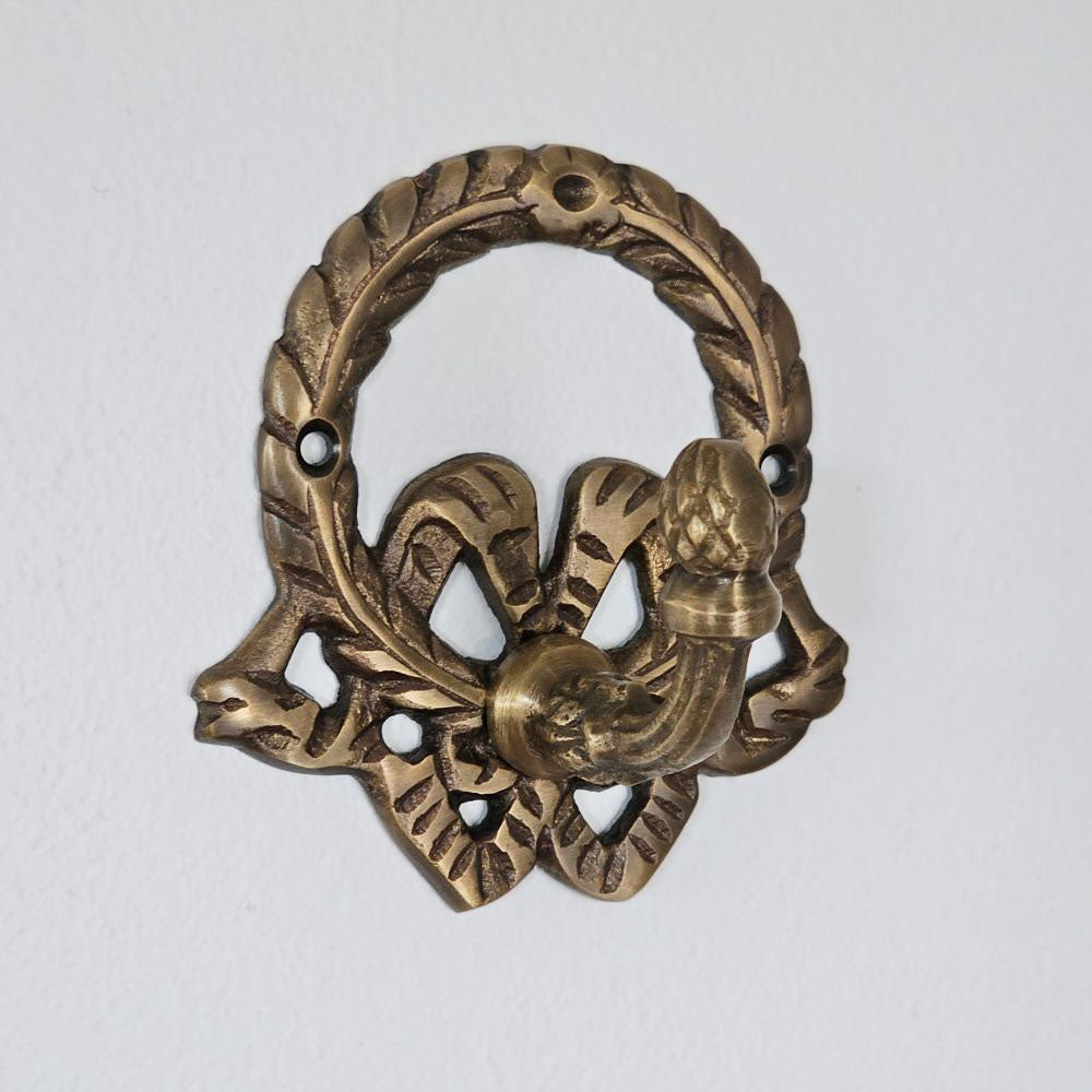 Add vintage old-world charm to any room with our Antiqued Brass Wreath Wall Hook. The aged brass finish and an ornate wreath design lends easy elegance to your home. Include two screws for hanging.