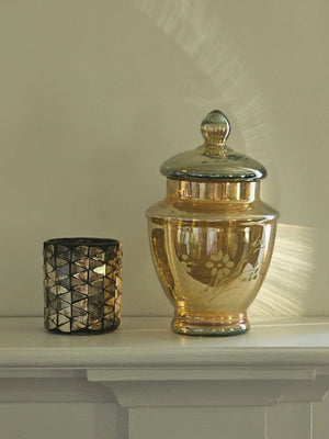 Add a magical touch to any space with our Iridescent Gold Glass Canister, a stunning decorative piece that brings vintage elegance and timeless charm to your home. The vintage-style mirrored glass finish catches and reflects light beautifully, creating an enchanting shimmer that transforms throughout the day. Etched with an intricate flower design on the front, this canister showcases thoughtful craftsmanship and old-world artistry. 