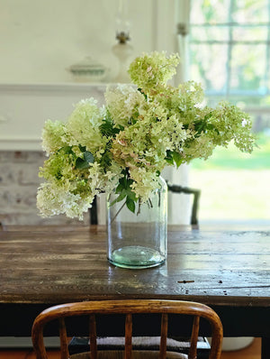 Our Recycled Glass Jar Vase features a green sea-glass look. Handcrafted from recycled glass, these rustic vases have a distinct, uneven texture and simple design. No two alike, size and color will differ slightly with each piece. Create a stunning farm table centerpiece, while bringing vintage and modern farmhouse style together with this oversized glass jar. Glass Jar only. Flowers not included. 6.7” diam x 12.6”H