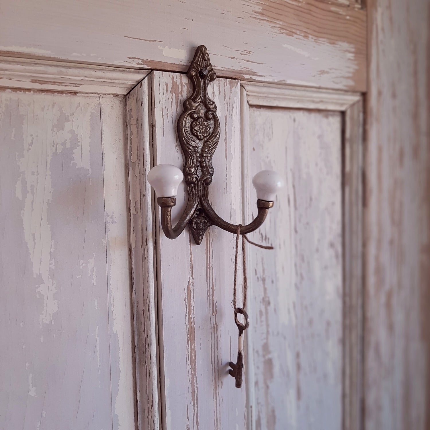 Add vintage old-world charm to any room with our Antiqued Brass Double Hook with Porcelain Knobs. This solid cast iron piece features and aged brass finish and an ornate floral design. Includes two hooks capped with vintage porcelain knobs.