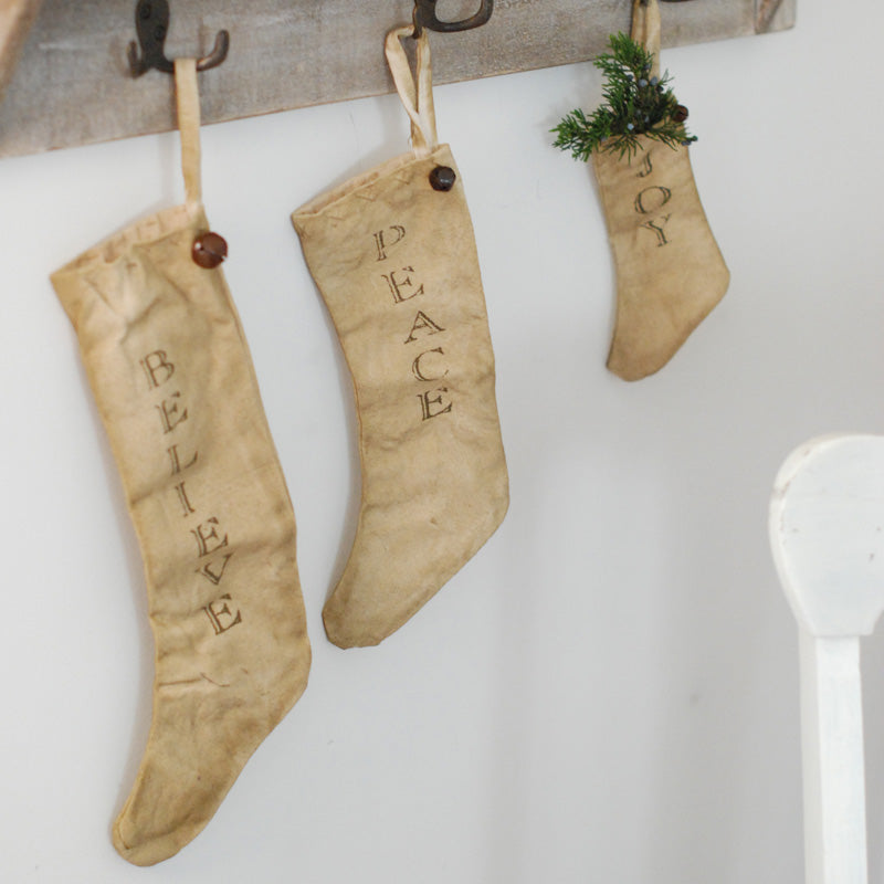 The warm, neutral tones of these cotton Country Christmas Stockings, each with rusted jingle bell, make this set of three an easy fit for farmhouse style holiday decor. Features a soft, oatmeal-color fabric along with the words Joy, Peace, and Believe for added charm.