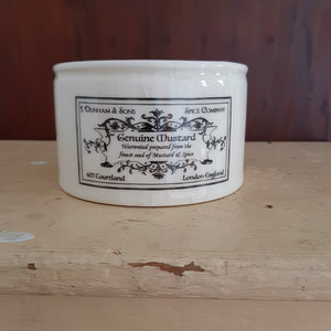 These handsome Ironstone Style Crocks are inspired by 19th century ironstone from potteries throughout England. These reproduction crocks have an oatmeal color with a decorative black logo. The creamery crock features a woman milking a cow. The smaller mustard crock features an old-timey logo.