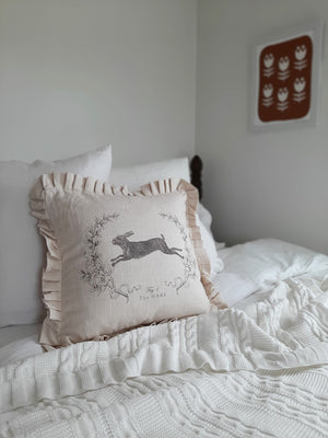 This Linen Style Hare Pillow with Ruffles lends a vintage charm to any room. Made of 100% cotton, this super soft pillow features a leaping bunny illustration on a rustic linen look fabric that has a warm oatmeal color. It instantly brings a cozy, down-to-earth sensibility to any farmhouse. The sweet ruffled edging lends a cottage feel.  Backside features a zippered closure. 100% cotton. 16"L x 16"H. Pillow insert made of 100% Polyester.