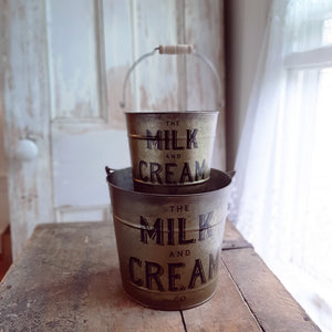 Whether you're gathering flowers from the garden, eggs from the chicken coop, or keeping your home organized, this set of two Milk and Cream Buckets will help get the job done. These galvanized buckets feature a rustic golden finish and vintage style wood handle grips. Perfect for utensils, flowers and so much more!
